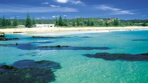 A beach with clear turquoise waters, rocky areas, and a forested background. - The Three Ways Alligator Creek (Alligator Creek)