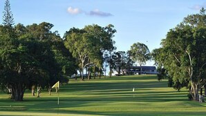A golf course with a flagstick, trees, and a building in the background. - The Three Ways Alligator Creek (Alligator Creek)