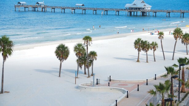 A beach with a pier, palm trees, and a building with a dome roof.
