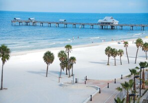 A beach with a pier, palm trees, and a building with a dome roof.
