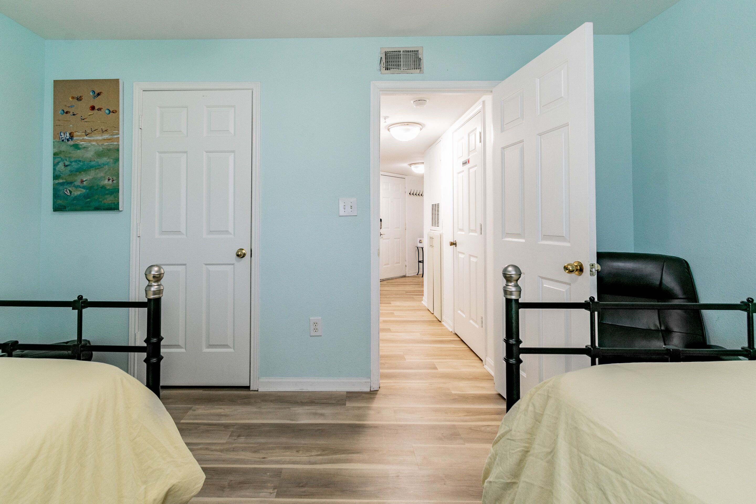 A room with two beds, a hallway, and a door leading to another room.