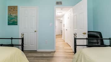 A room with two beds, a hallway, and a door leading to another room.
