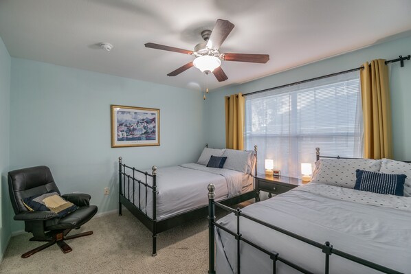 A bedroom with two beds, a chair, a ceiling fan, and a window with curtains.