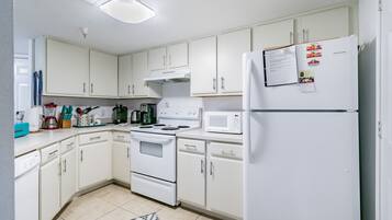 A kitchen with white cabinets, a stove, a microwave, and a refrigerator.