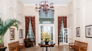 A spacious lobby with a round table, two wooden benches, a potted plant, and a chandelier.