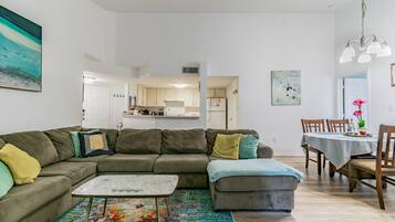 A modern living room with a sectional sofa, a coffee table, and a dining area with a table and chairs.