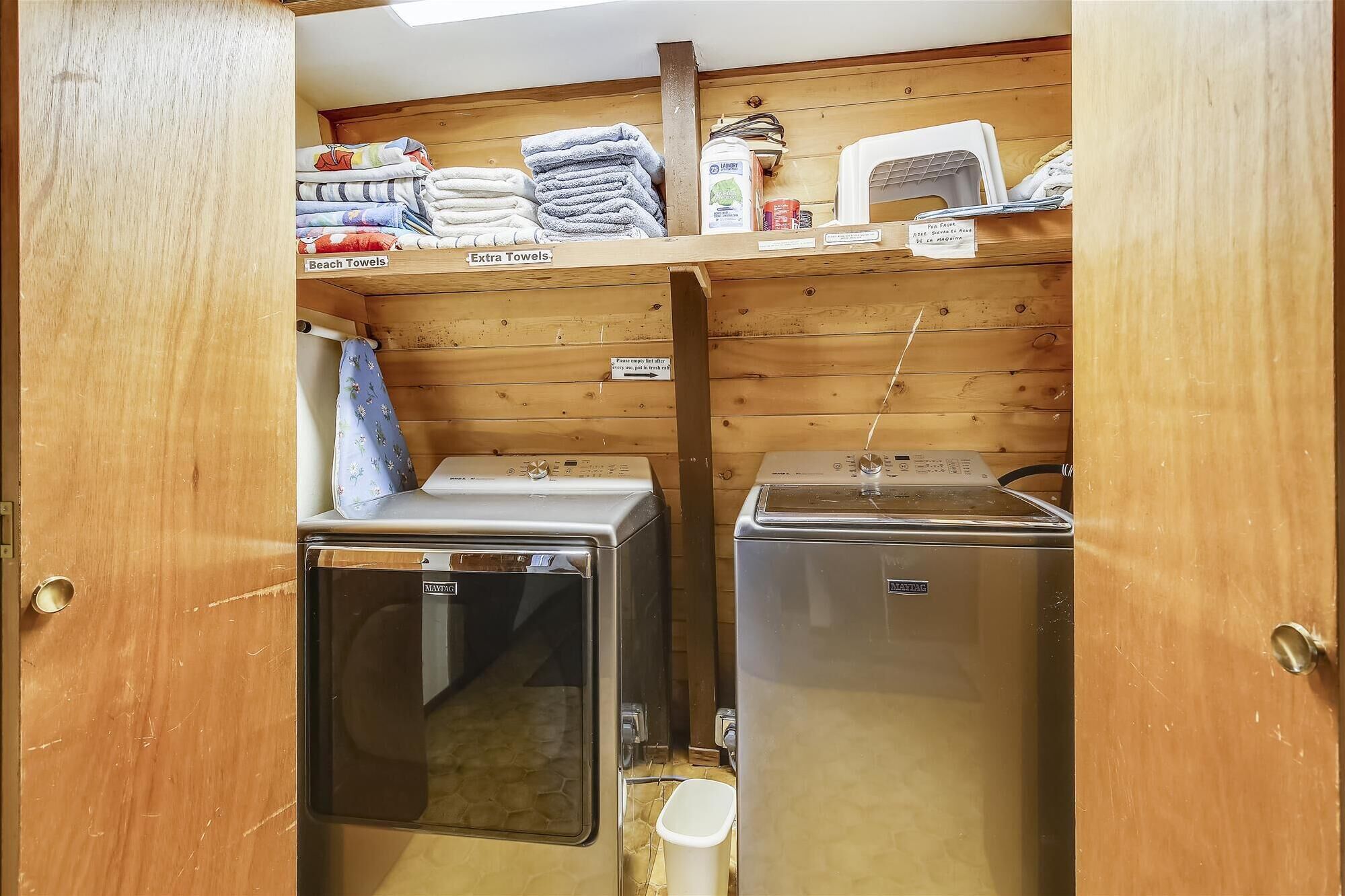 A compact laundry room with two washing machines, a shelf with towels, and a laundry detergent bottle.