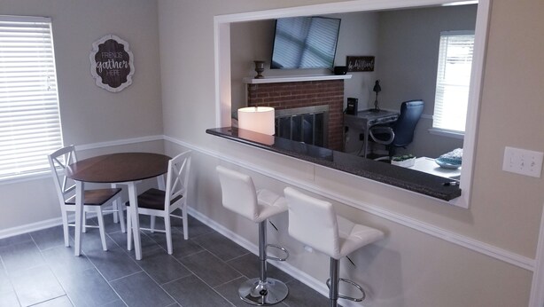Una zona de comedor con una mesa redonda y cuatro sillas, una barra con dos taburetes, un televisor montado sobre la barra y una chimenea.