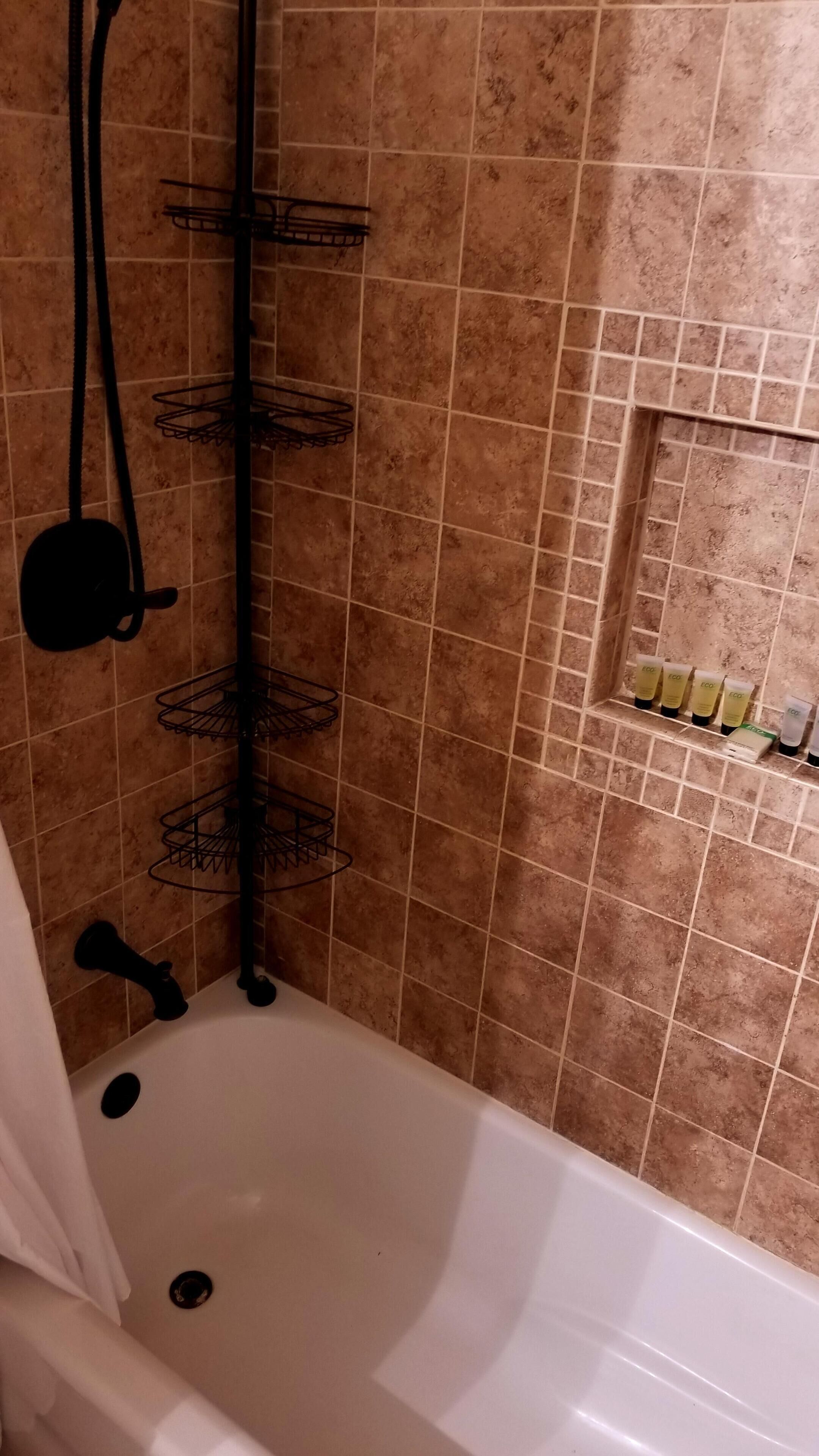 A bathroom with a bathtub, a shower area with a metal rack, and a shelf with toiletries.