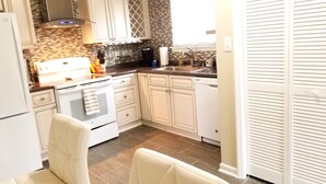 Una cocina con muebles blancos, estufa, pileta y una encimera con varios objetos.