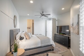 Relax in this serene bedroom featuring a large bed with a tufted headboard, flat-screen TV, and ceiling fan.