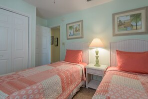 A bedroom with two beds, each with a matching headboard and pillow, a bedside table with a lamp, and framed artwork on the walls.