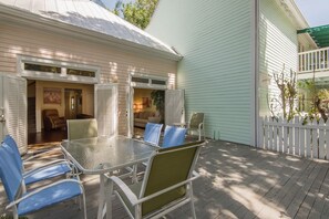 A covered patio with a glass table and chairs, a white fence, and a light blue building.