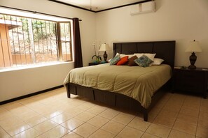 Un dormitorio con una cama, dos mesitas de noche, una ventana con cortinas y un aire acondicionado instalado en la pared.