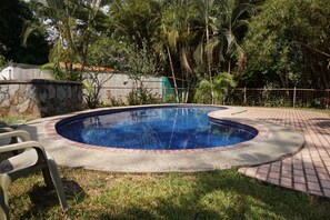 Piscina com borda de tijolos, cercada por grama e árvores.
