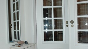 Eine weiße Tür mit Glasfeldern, ein Spiegel über einem kleinen Schminktisch mit Ablage, und ein gefliester Boden.