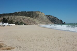 A beach with a rocky cliff and a building in the background. - Modern Comfortable Apartment, Sleeps 3. (Praia da Luz Lagos)