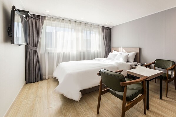 A hotel room with a bed, a desk, two chairs, a flat-screen TV mounted on the wall, and a large window with sheer curtains. - Anyang ILLOWA Hotel (Anyang)