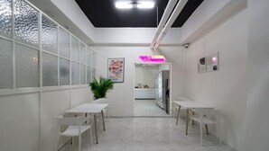 A modern, minimalist room with white walls and a glass partition. There are two white tables with chairs, a potted plant, and a neon sign. - Anyang ILLOWA Hotel (Anyang)