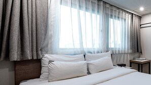 A hotel room with a bed, white bedding, a nightstand with a phone, and sheer curtains over a window. - Anyang ILLOWA Hotel (Anyang)