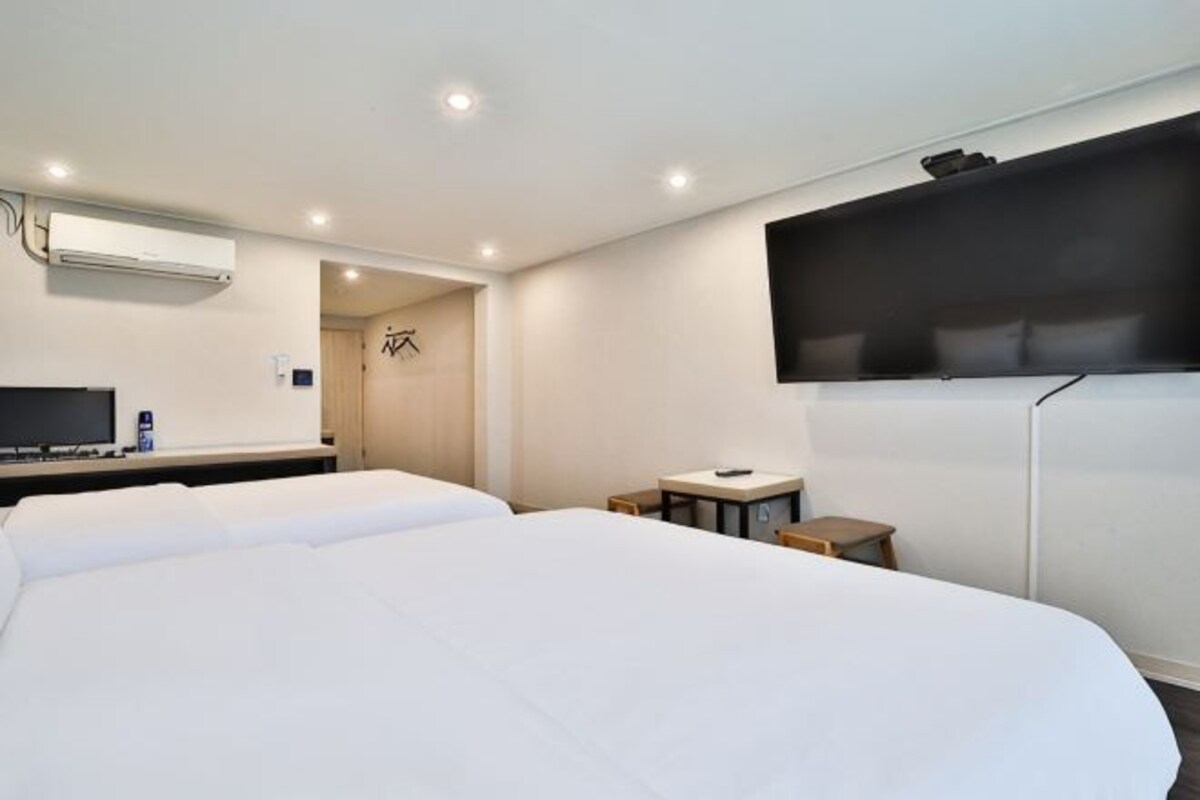 A hotel room with a large bed, a desk, a chair, a TV, and a wall-mounted TV.