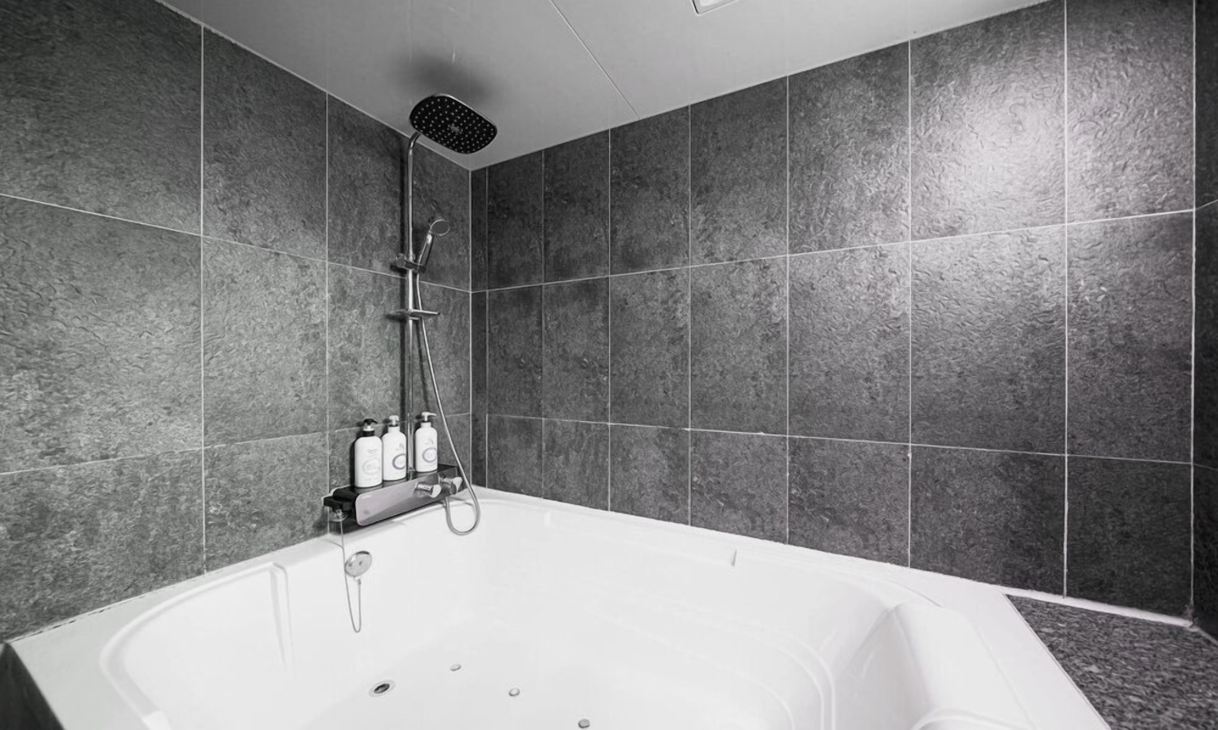 A modern bathroom with a freestanding bathtub, a handheld showerhead, and a wall-mounted faucet.