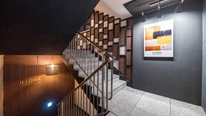 A modern staircase with a wooden handrail and metal balusters, leading to a landing with a wall-mounted light fixture and a framed artwork. - Anyang ILLOWA Hotel (Anyang)