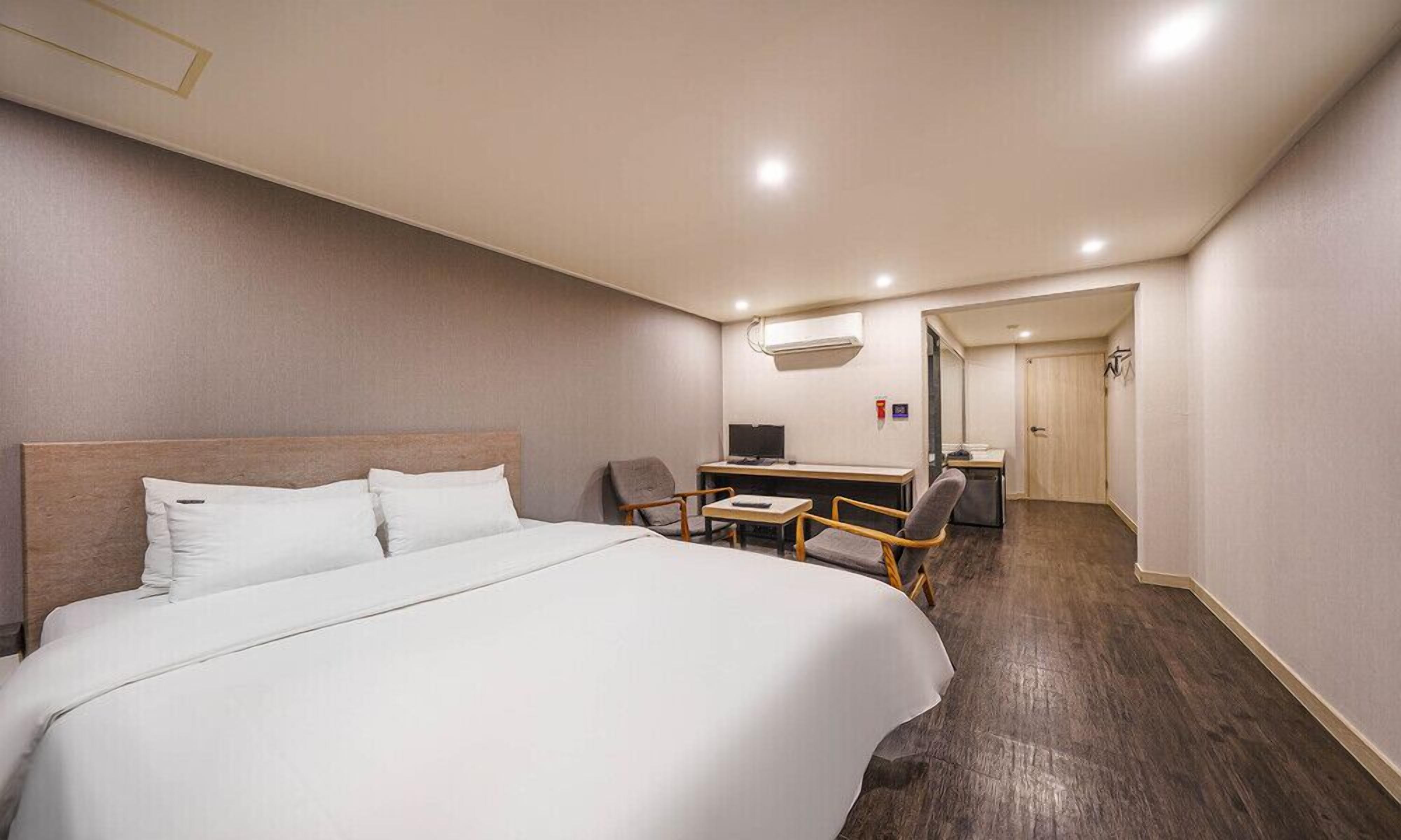 A hotel room with a large bed, a desk with a chair, a TV, and a small kitchenette.