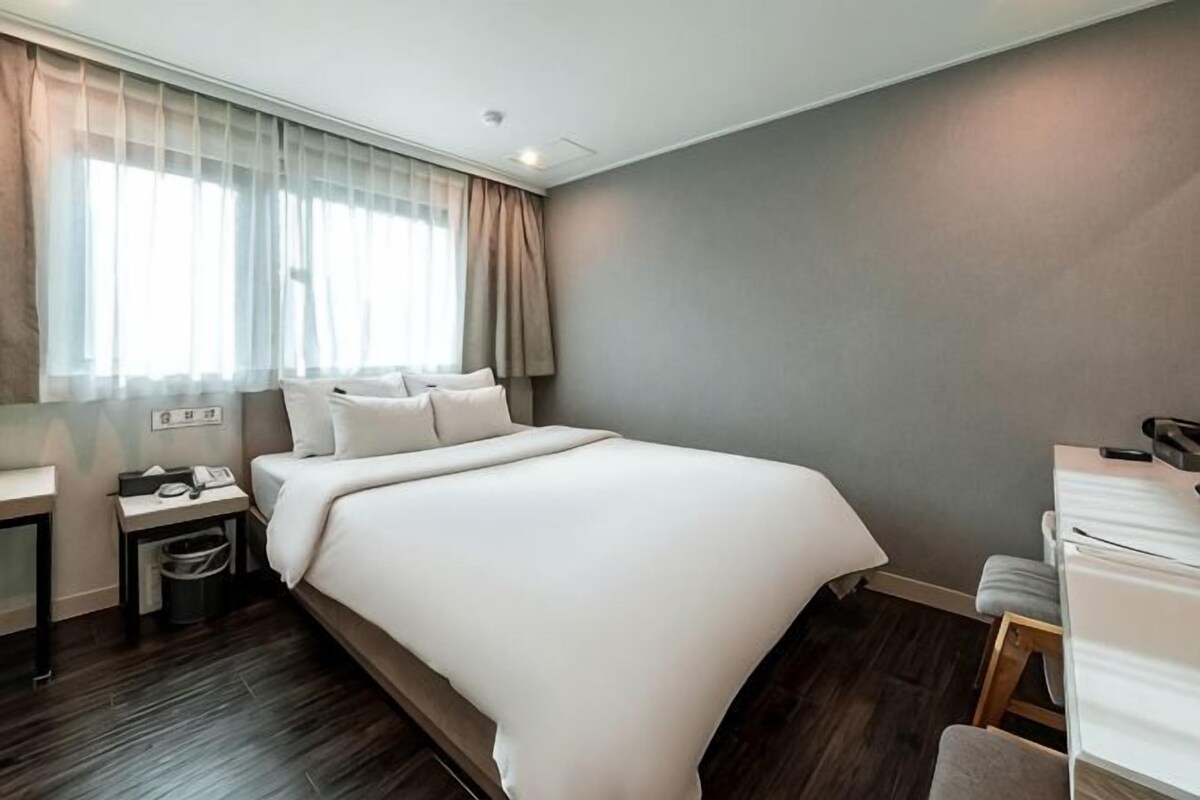 A hotel room with a large bed, bedside table, and a desk with a chair.