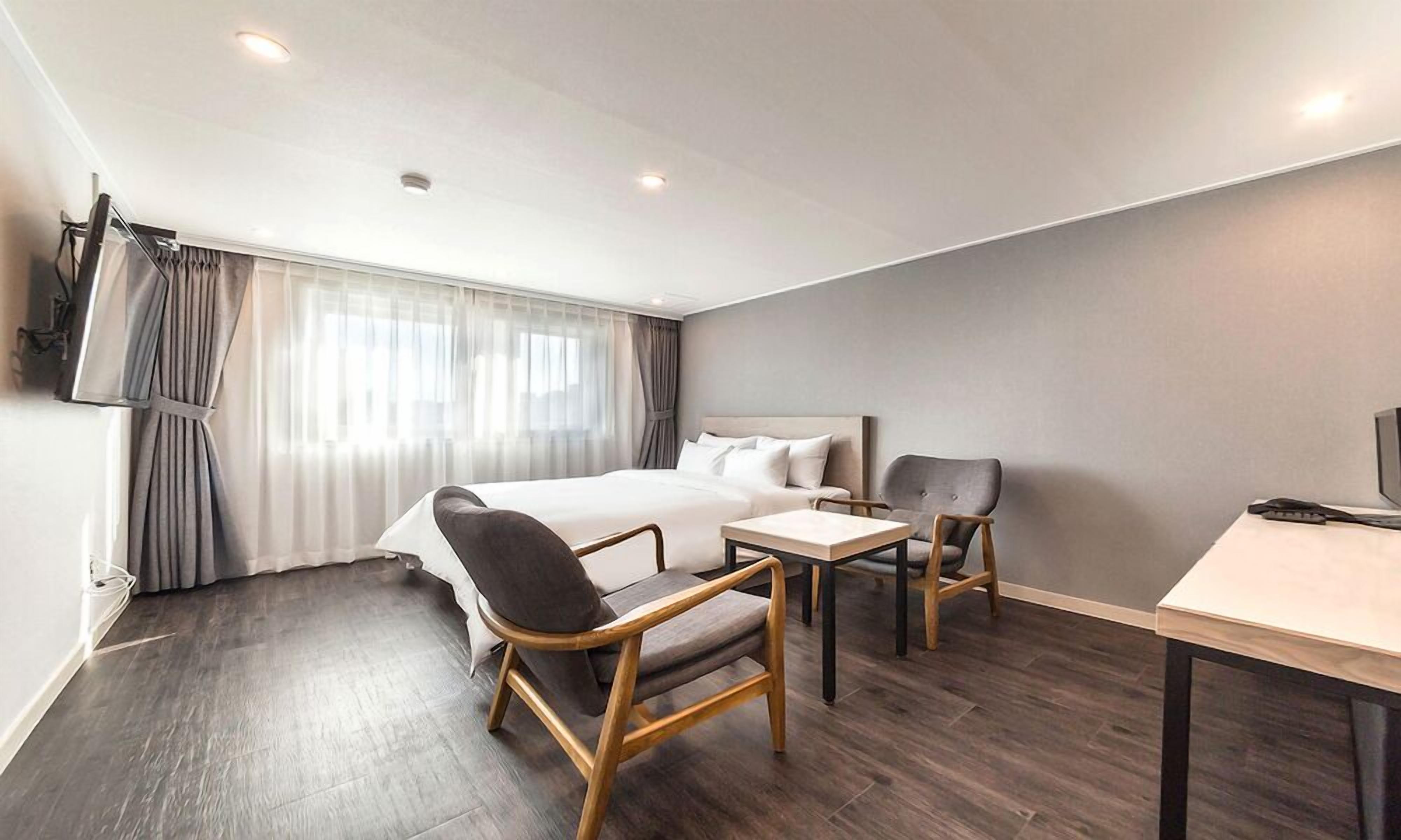A modern hotel room with a large bed, a desk, two chairs, and a television.