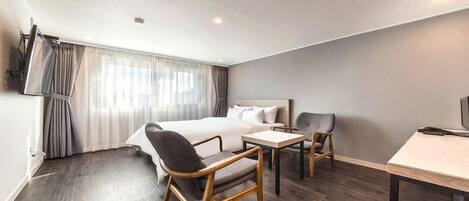 A modern hotel room with a large bed, a desk, two chairs, and a television.