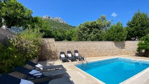 A swimming pool with lounge chairs and a stone wall. - Seafront Historic Villa | Private pool, kayaks and bikes (Viganj)