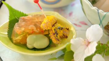 A plate with various food items, including a translucent jelly-like dish, a yellow crumbly item, and a green oval-shaped item, all on a green leaf.