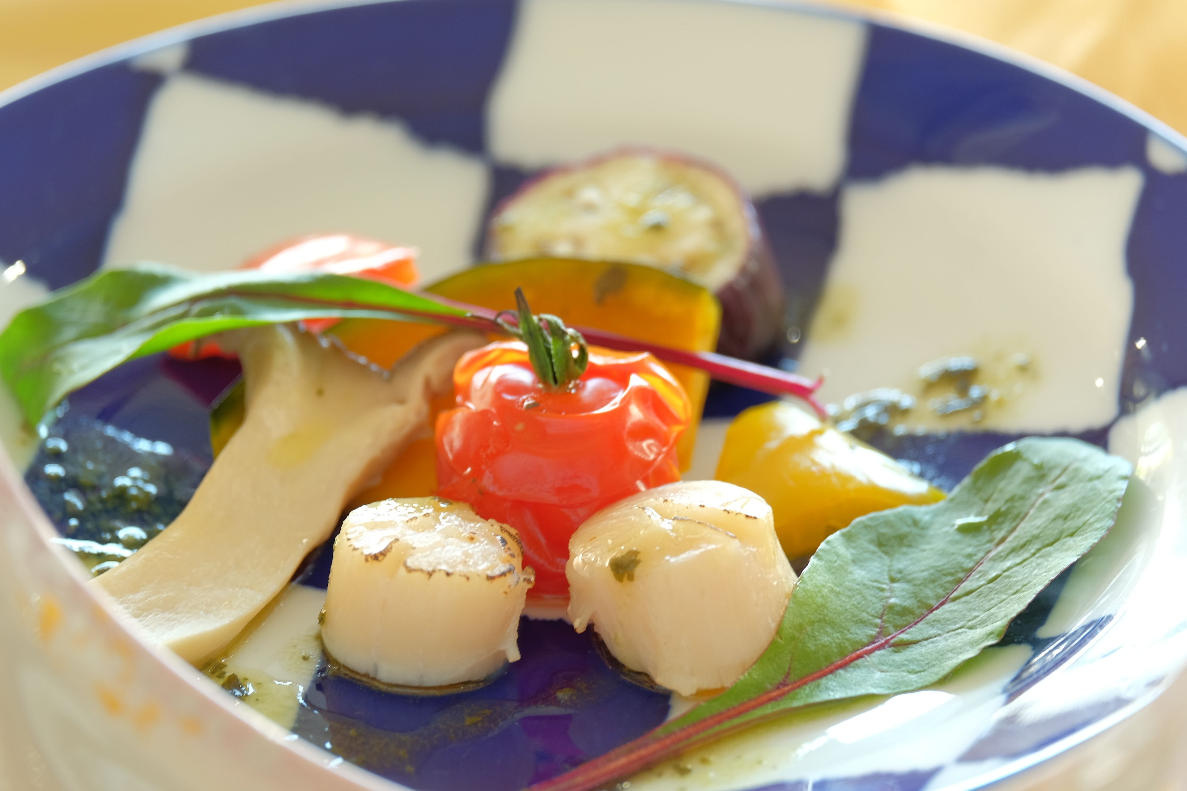 A plate with a variety of vegetables and a piece of meat, possibly scallops, on a blue and white checkered plate.