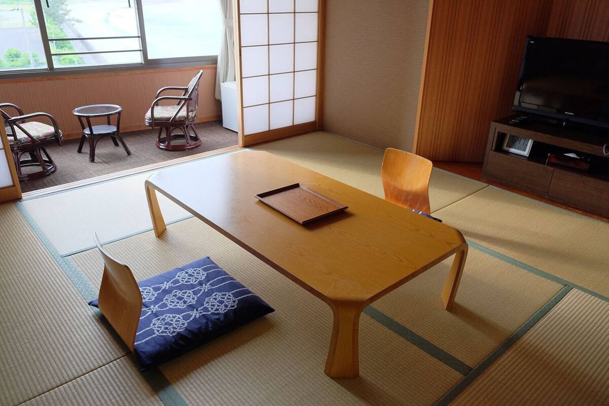 Una habitación tradicional japonesa con suelo de tatami, una mesa de madera baja y un televisor sobre un soporte de madera.