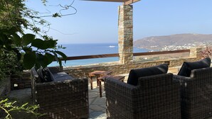 A patio with wicker furniture and a stone pillar, overlooking a coastal view with a ship in the distance. - Breathtaking Panoramic Sea View.Private swimming pool  4,5 m X 11 m! (Kato Agios Petros)