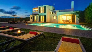 Ein modernes, zweistöckiges Haus mit Pool, Sitzgelegenheiten im Freien und einer gut beleuchteten Terrasse.
