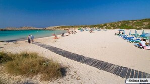 Ein Strand mit gepflastertem Weg, Liegestühlen und Sonnenschirmen.