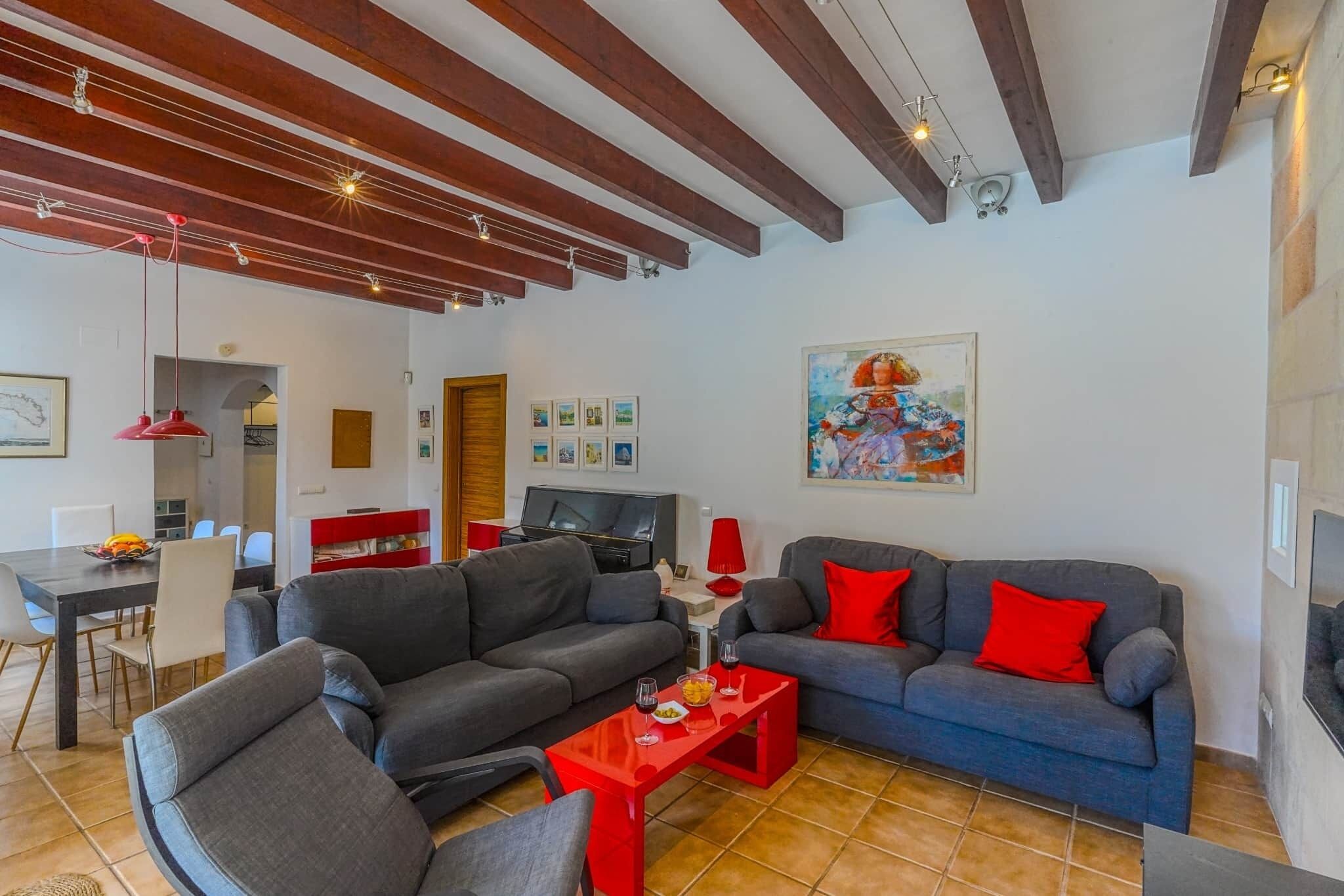 A living room with two grey sofas, a red coffee table, and a TV. There are red and white walls, a wooden ceiling, and a painting on the wall.
