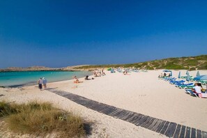 A beach with a paved walkway, beach chairs, and umbrellas.