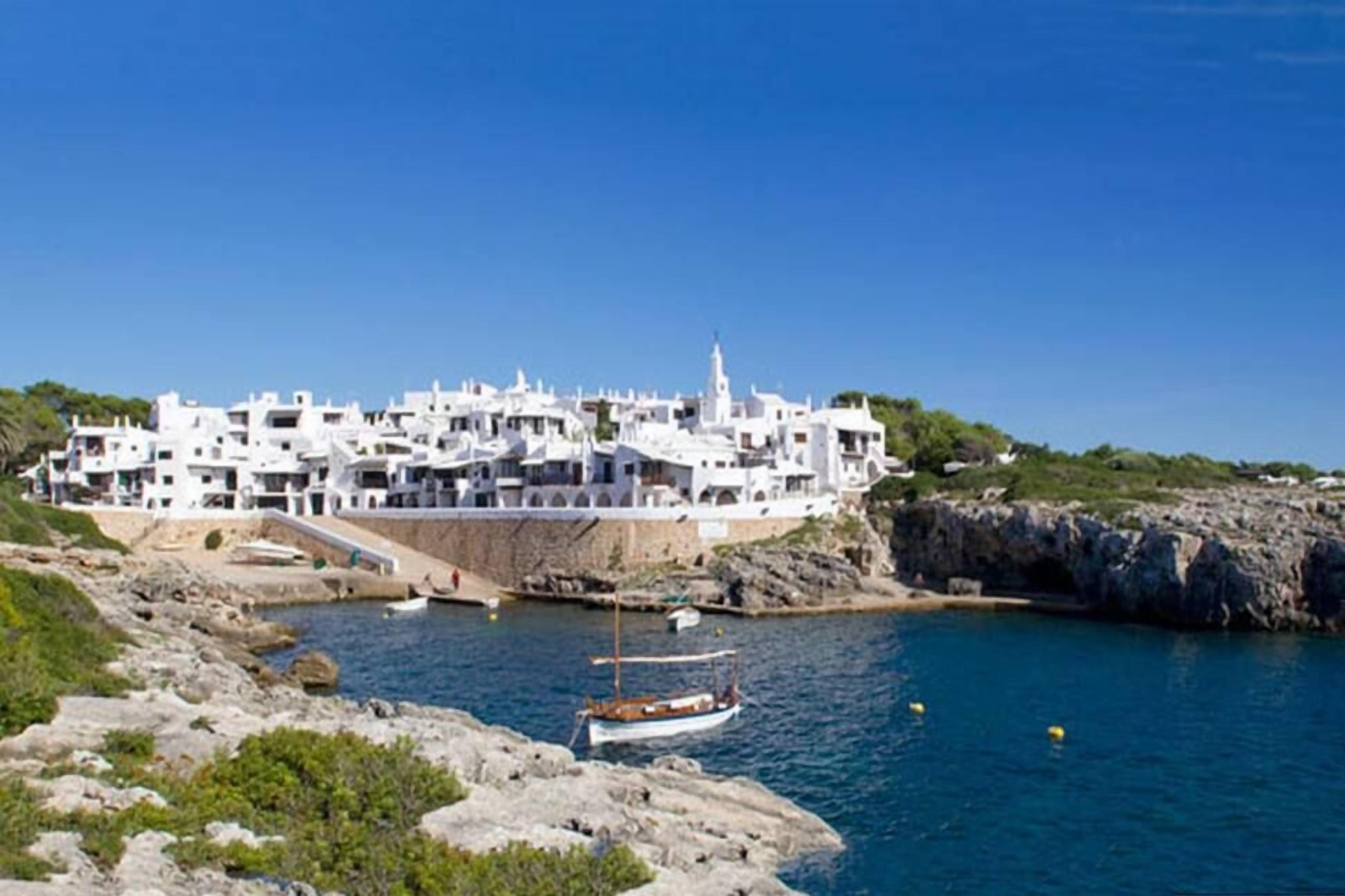 Une ville côtière aux bâtiments blancs, avec un littoral rocheux et un bateau sur l’eau.