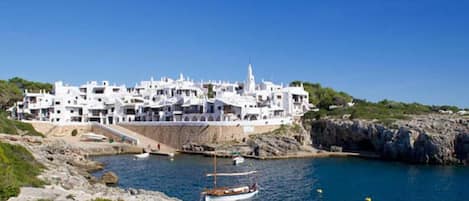 Un pueblo costero con edificios blancos, una costa rocosa y un bote en el agua.