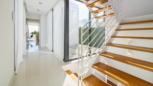 A modern staircase with wooden steps and white railings leading to a glass door. - Designer Alcanada by Balearic Villas (Alcúdia)