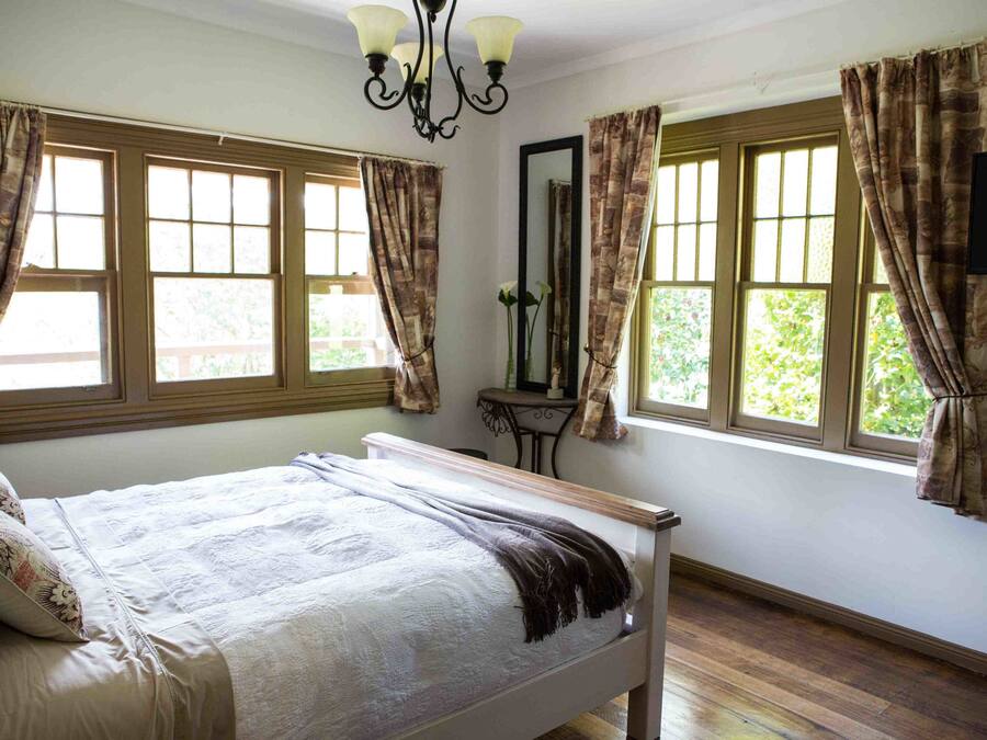 Ein Schlafzimmer mit Bett, Vorhängen, einem Spiegel und einem Fenster.