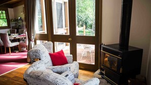 A cozy living room with a sofa, a fireplace, and a dining area visible through a glass door. - Buttercuphill B&B (Warburton)