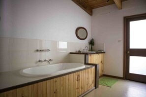 A bathroom with a wooden vanity, a bathtub, a mirror, and a green mat on the floor. - Buttercuphill B&B (Warburton)