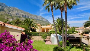 Een villa in mediterrane stijl met een stenen muur, palmbomen en een berg op de achtergrond.