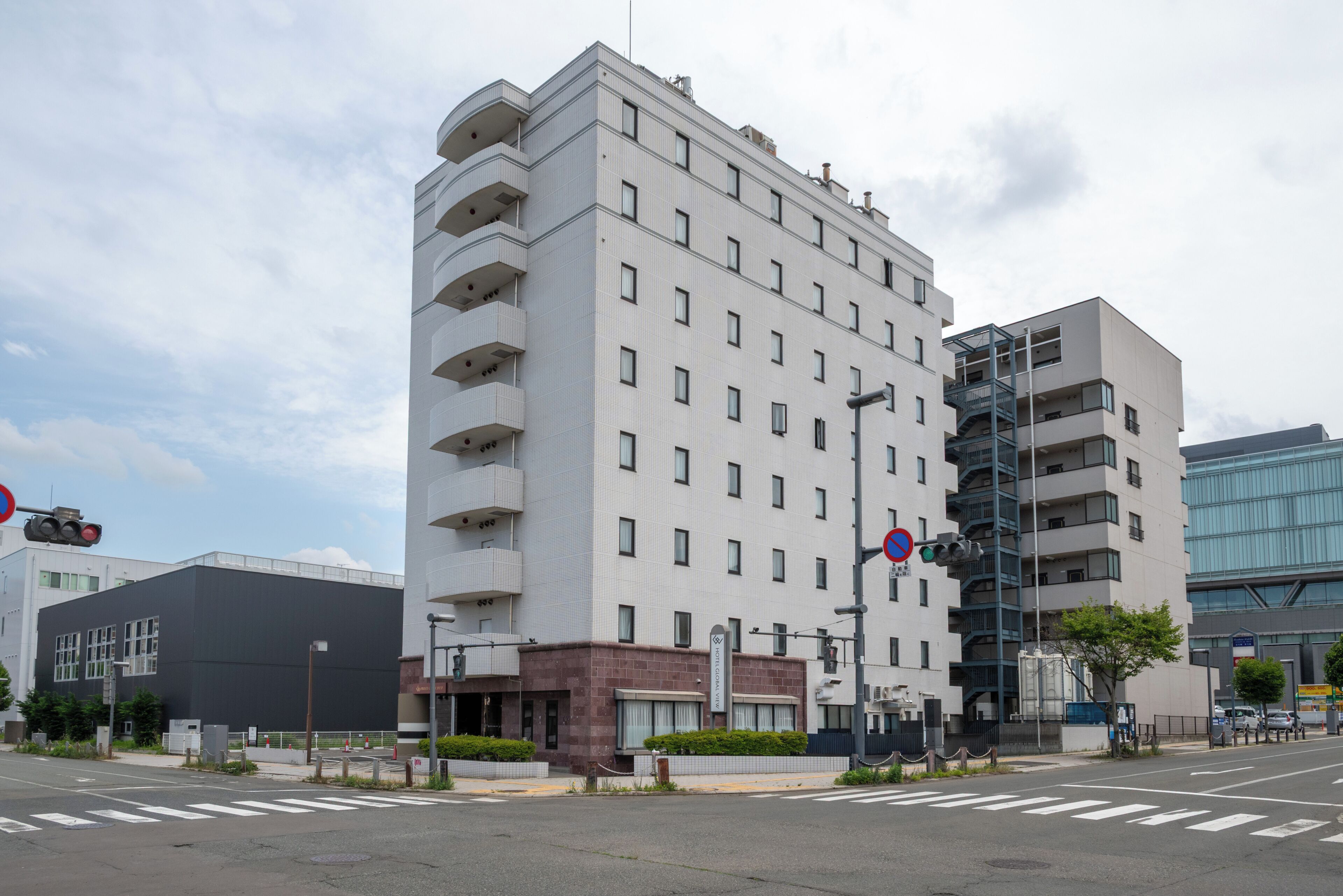 Et moderne hotel med flere etager, med altaner på hver etage, en tydelig indgang og en parkeringsplads foran.