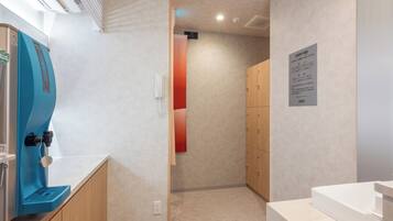 A hotel room with a blue water dispenser, wooden cabinets, a white sink, and a beige carpet.