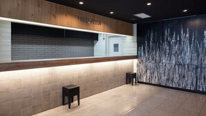 Un espace d’accueil avec un panneau en bois, un comptoir de réception, une porte blanche et un mur à texture.